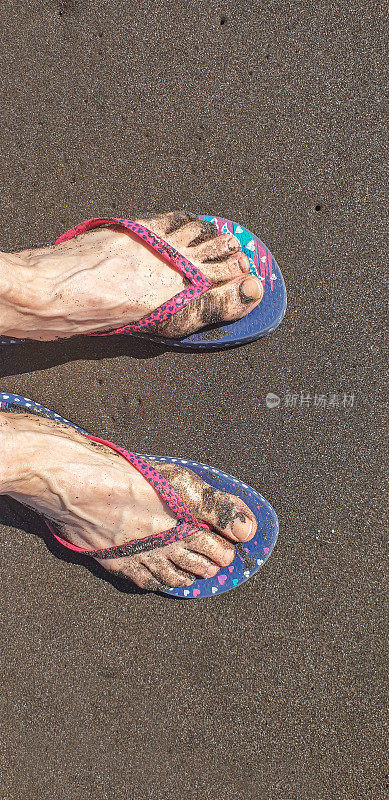 穿着人字拖的女性脚踩在沙滩上