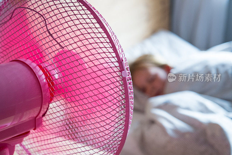 女孩睡在床上，粉红色的扇子吹着凉爽的空气