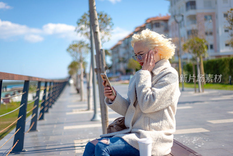 震惊的年轻女子的肖像看着智能手机的屏幕，带着悲伤的表情