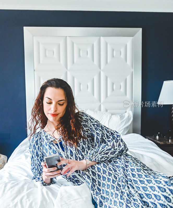 女人在家里躺在床上放松，漫不经心地用手机进行FaceTime或视频聊天