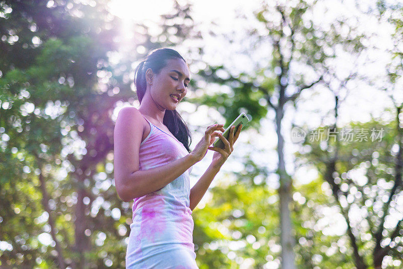 一个美丽的和好看的年轻亚洲女性模特女士穿着五颜六色的夏天冷连衣裙在公园的手机