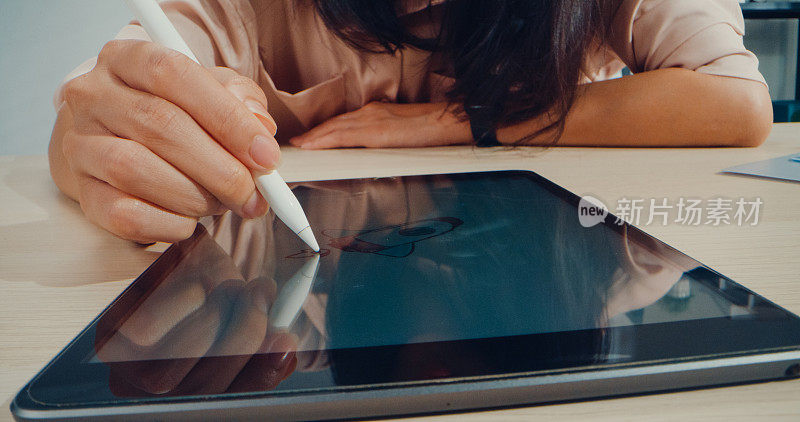 在办公室工作的年轻亚洲女性写数字平板电脑的手的特写。