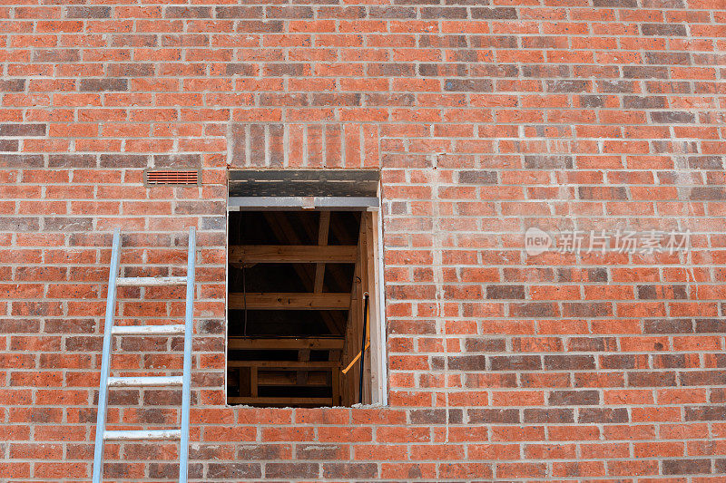 一架靠在红砖墙上的铝梯子通向一座新建房屋的空窗户