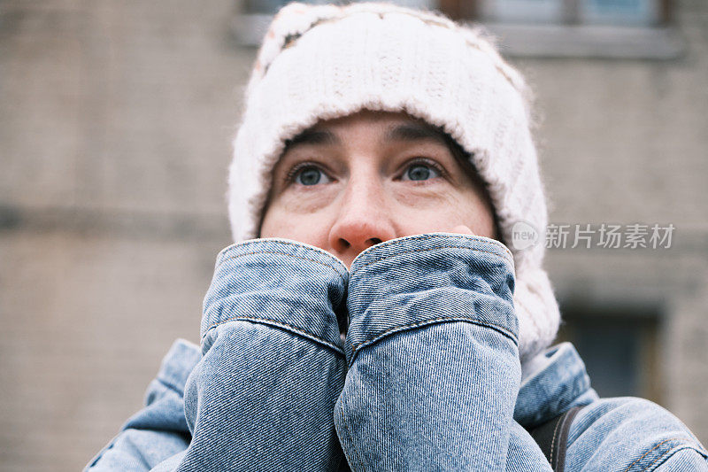 在寒冷的城市街道上，一名妇女正冻得双手发热