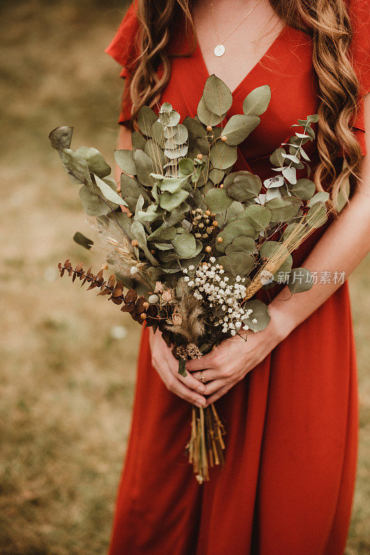 身穿红裙的伴娘手持干花束