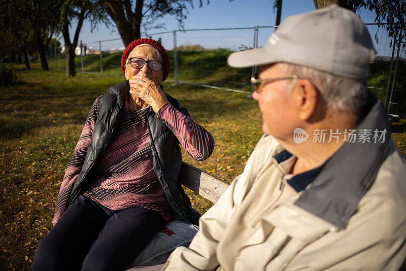 年长的女人和男人，坐在公园的长凳上，在秋日聊天