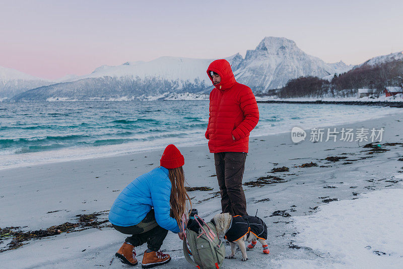 一对幸福的夫妇和一只狗在挪威风景优美的峡湾海滩上考虑冬季野餐