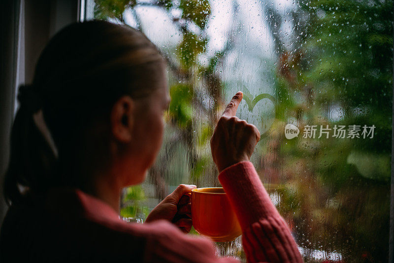 一个女人在雨天喝咖啡，在窗户上画心