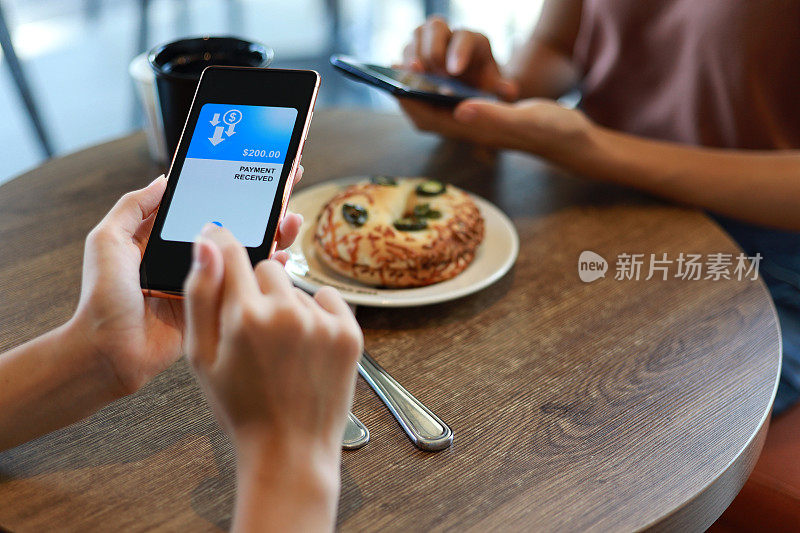 朋友们在咖啡馆共进早餐时，通过智能手机上的数字钱包应用程序分摊账单，发送和接收餐费的桌面视图。有技术的智能银行。