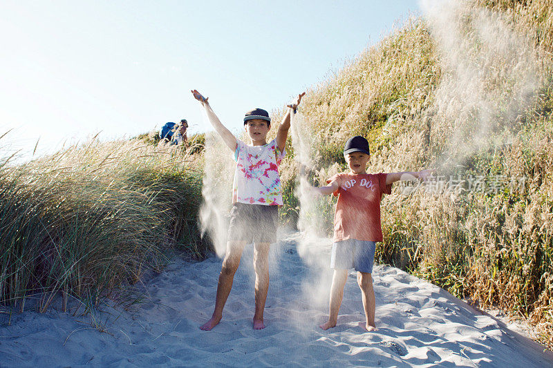 男孩们在海滩上向空中扔沙子