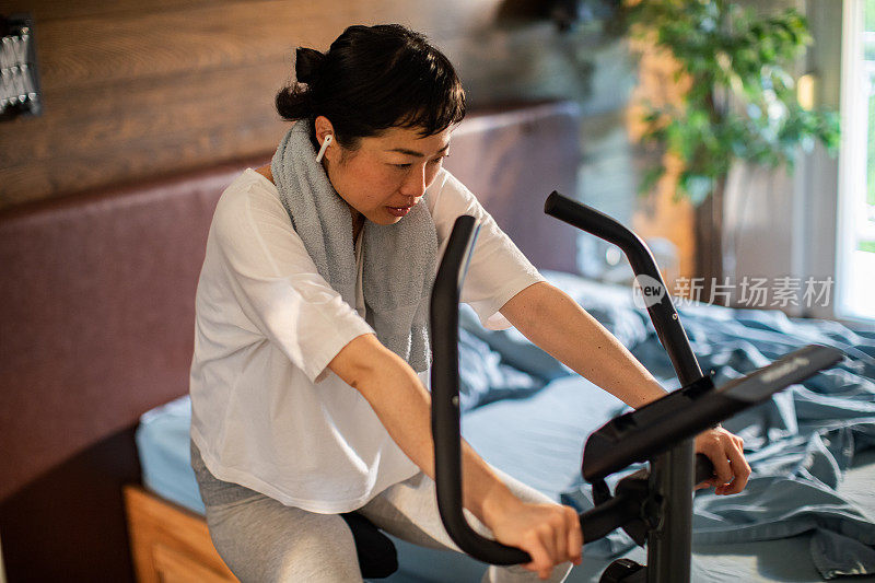 年轻的日本女子在卧室里骑室内自行车锻炼