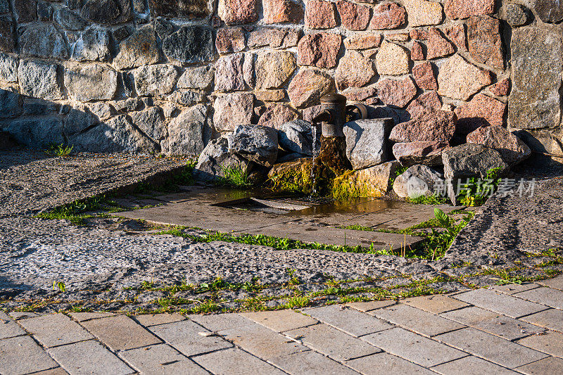 水从铺满砖石的街道上的泉水龙头流出