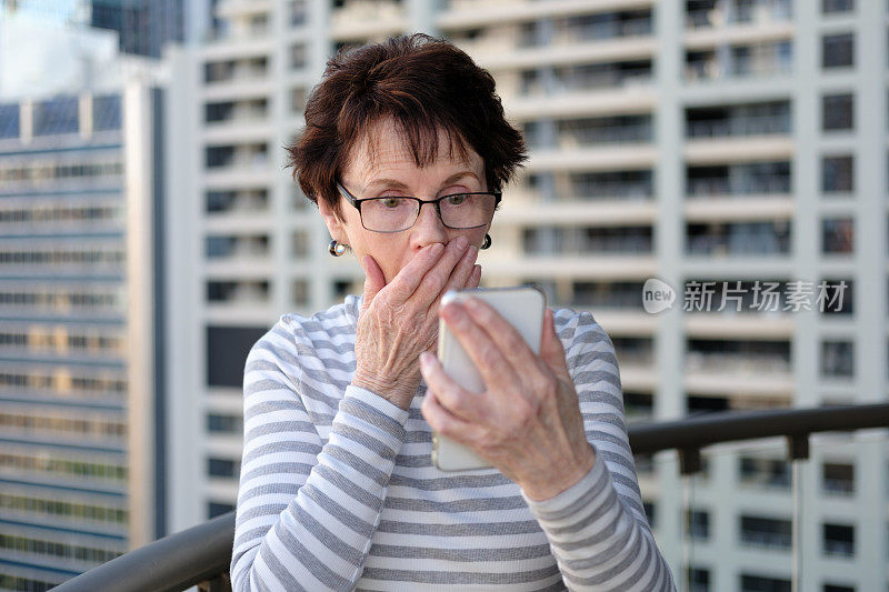 一位资深女性带着震惊的表情看着她的手机