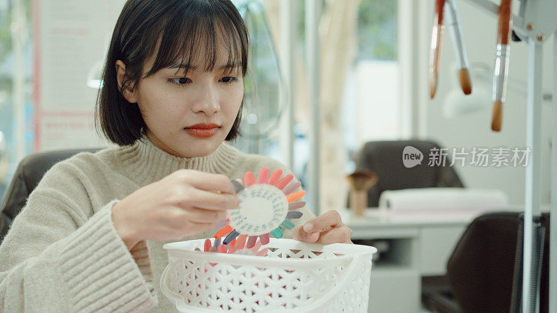 年轻的亚洲女性顾客在美甲美容院挑选指甲油色板，修指甲