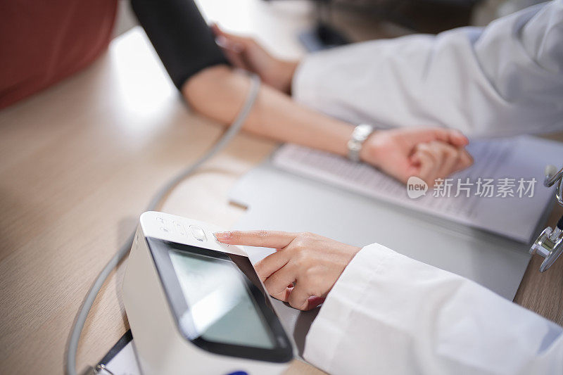 亚洲心理学家女性在诊所使用数字血压计测量女性患者的血压和心率，同时提供药物和心理健康治疗方面的咨询
