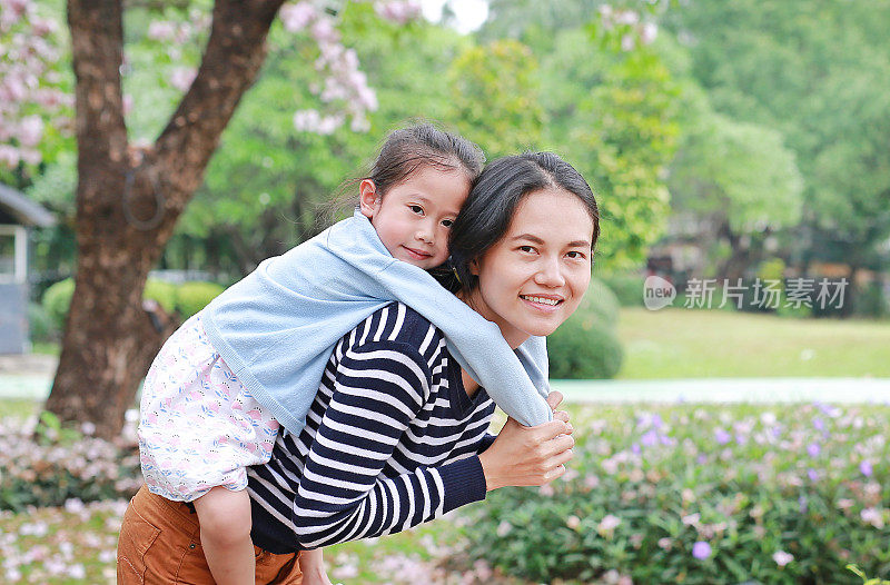 快乐的母亲抱着她的女儿在满是粉红色花朵的花园里。幸福美满的家庭。
