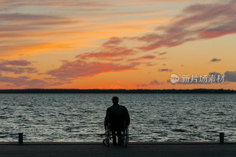 后视图老人坐在轮椅上看着雄伟的云在湖面上的晚霞