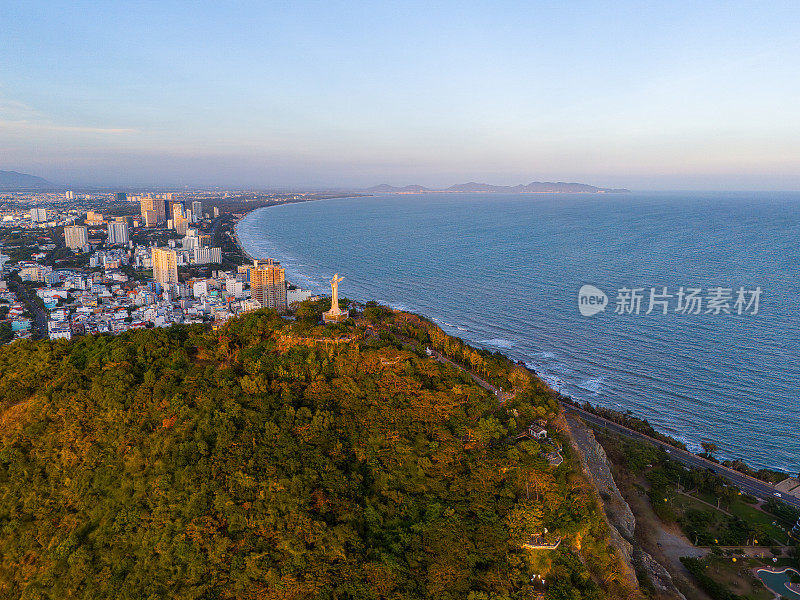 从上面俯瞰云头海岸全景，海浪、海岸线、街道、椰子树、越南Nho山后面的基督国王雕像