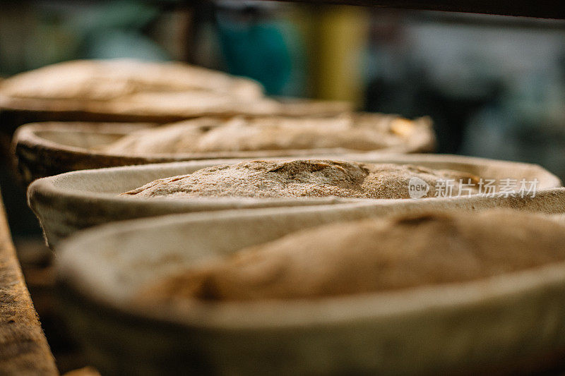 烤面包。面团放在木桌上的打样篮里，与面粉、孜然和麦穗放在一起。前视图。