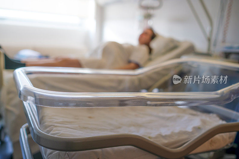 孕妇躺在医院的病床上，前景是婴儿床