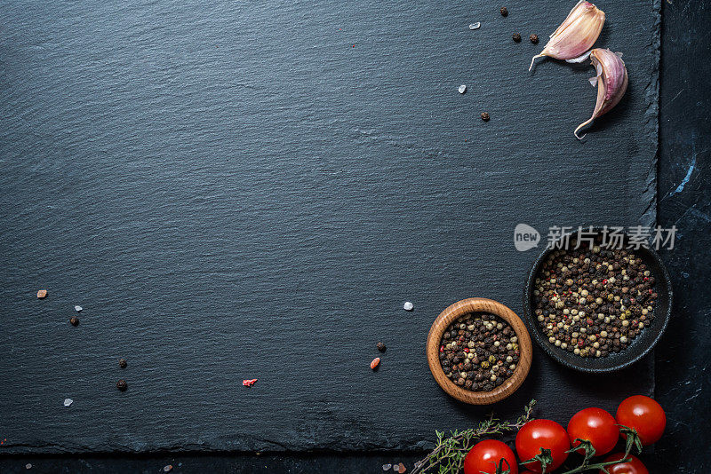 黑色石板餐盘，装饰有番茄，干胡椒调味料，大蒜和百里香。