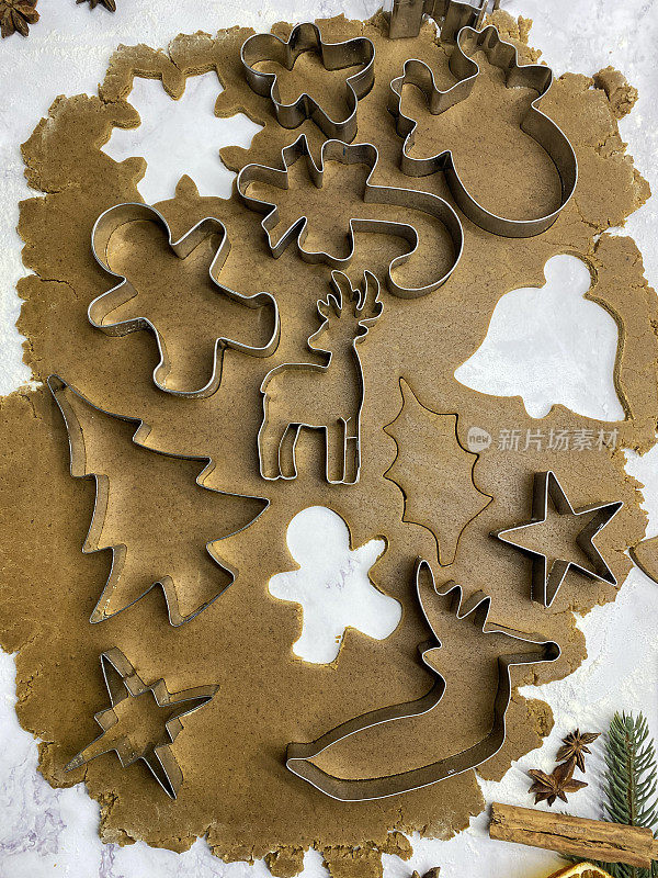 自制的图像，姜饼曲奇面团滚在大理石效果的背景上，金属圣诞主题饼干切割器，圣诞树，星星，驯鹿，糖果拐杖和姜饼人切割形状，家庭烘焙，高架视图