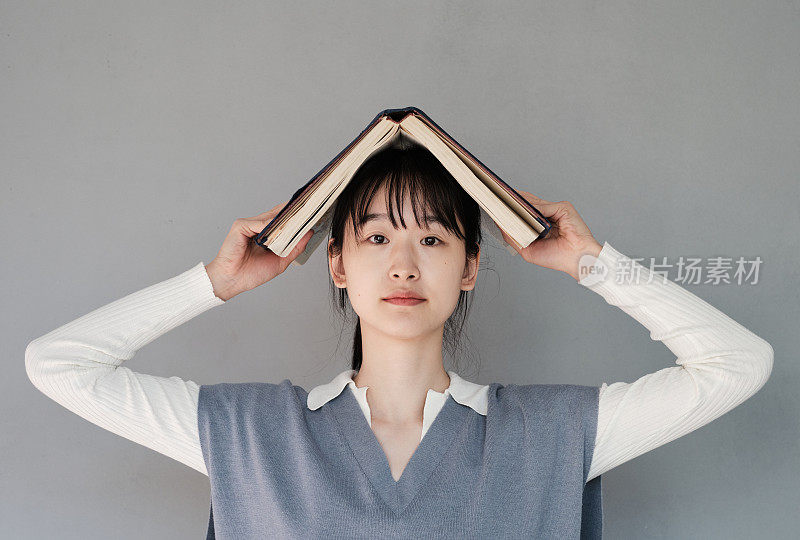 严肃的亚洲学生女孩的肖像与刘海站在书上对灰色背景