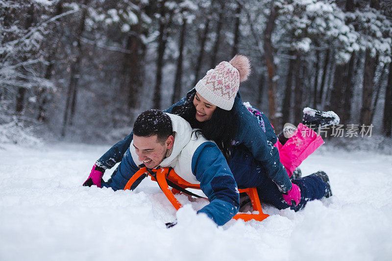 年轻美丽浪漫的夫妇躺在雪橇上在雪地里玩得很开心