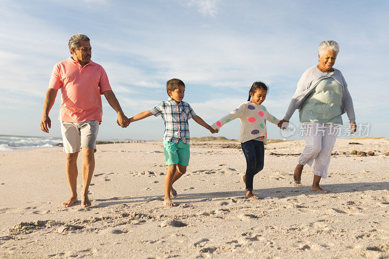 全长的年长混血儿男人和女人手牵着孙子在海滩散步