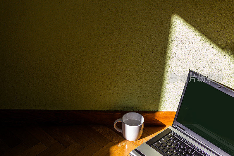 陶瓷马克杯和笔记本电脑在木地板上照明的自然光。概念:在家工作，休息一下