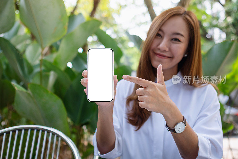 一个年轻女人拿着一个空白屏幕的手机，用手指指着它
