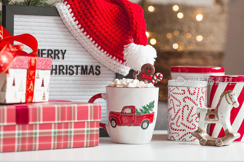 一个标志，上面写着:圣诞快乐，礼物，圣诞老人帽，热可可杯，棉花糖和姜饼人，背景是一个美丽的bokeh。温馨的新年和冬季假期概念