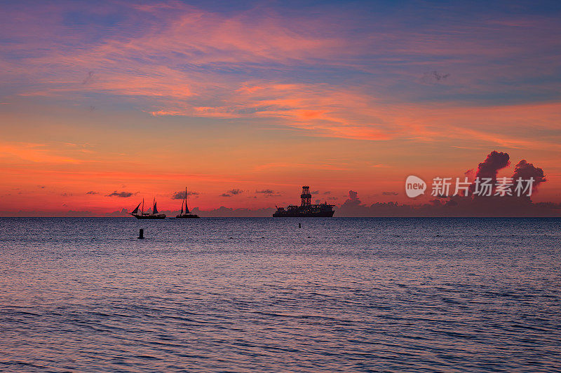 日落之后，在加勒比海的阿鲁巴西海岸。地平线上帆船和石油勘探船的剪影