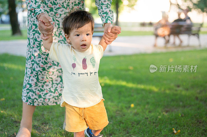 一岁大的孩子在妈妈的帮助下在公园里迈出了第一步