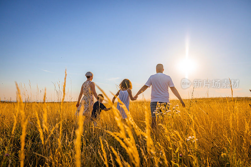 在黄金时间，一家人一起在草地上散步，背对着天空