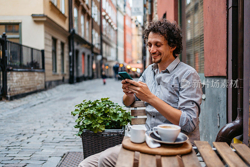 一个年轻人在人行道上喝咖啡和使用手机Café