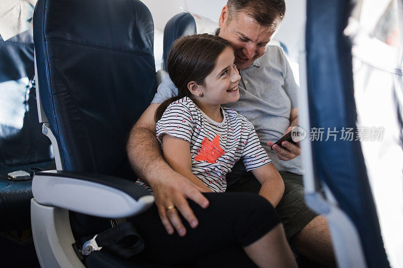 父亲和女儿在飞机上使用智能手机