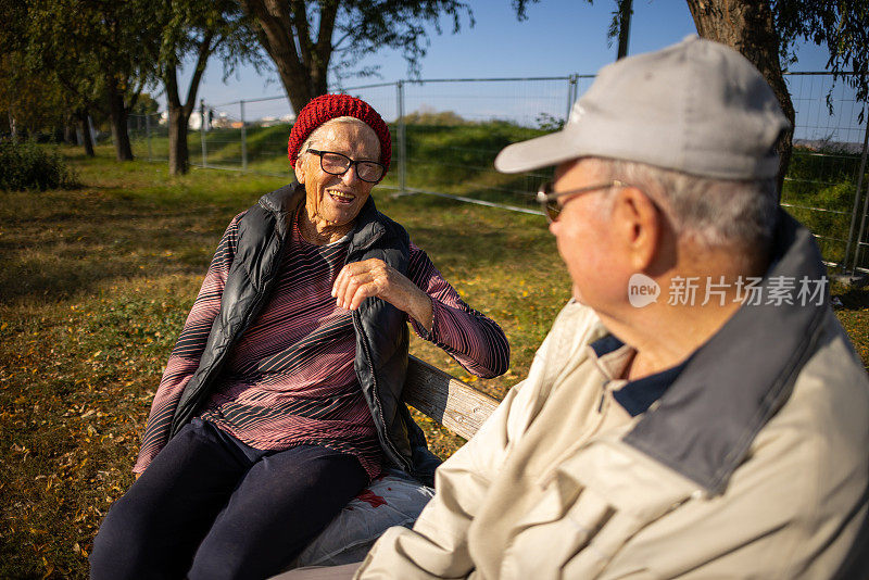 年长的女人和男人，坐在公园的长凳上，在秋日聊天