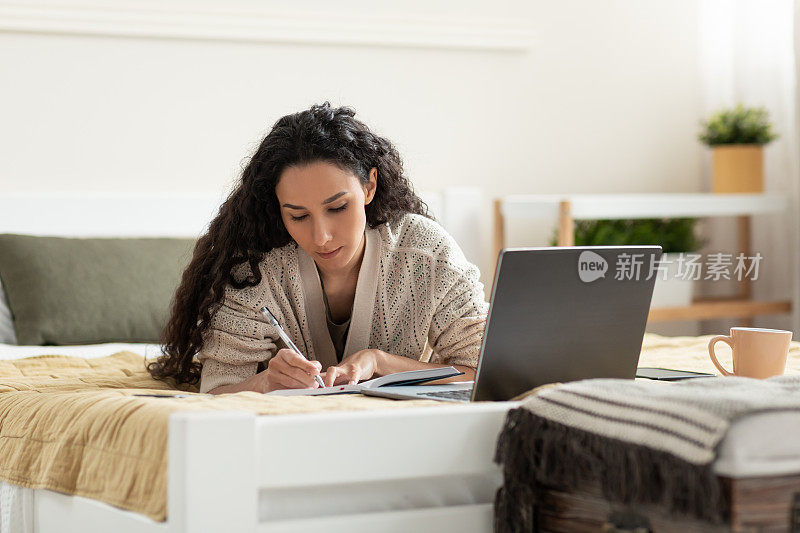 专注的年轻女性使用笔记本电脑，在线工作或学习，在商业会议或网络研讨会期间在家做笔记