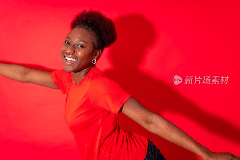 年轻的非裔美国妇女被孤立在红色背景上，微笑着跳舞，摄影棚拍摄