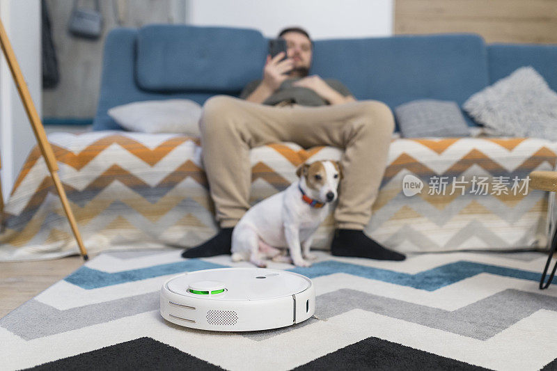 一对夫妇坐在沙发上，带着狗在家里用真空机器人清洁地板