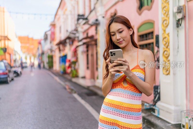 Z世代亚洲女性在旅行中使用智能手机探索普吉岛旧城的魅力，随时随地连接社交媒体。年轻女子与设备互动。通过设备连接生活方式。