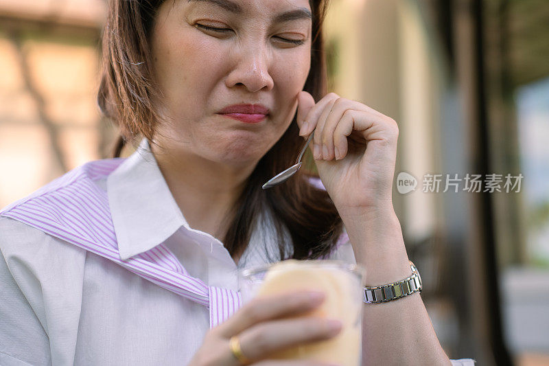 亚洲妇女用勺子吃冷甜点，以减轻牙齿敏感引起的疼痛，面部表情焦虑。