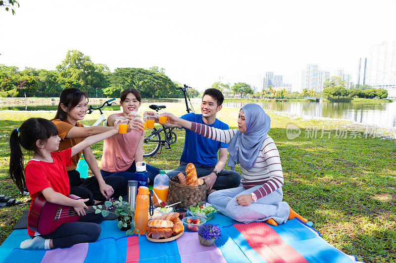 亚洲的家人和朋友一起坐在毯子上，吃着水果和饮料，在公园里野餐
