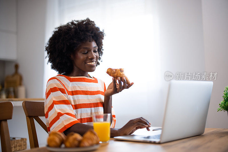 一名非洲裔美国年轻女子边吃午饭边用笔记本电脑