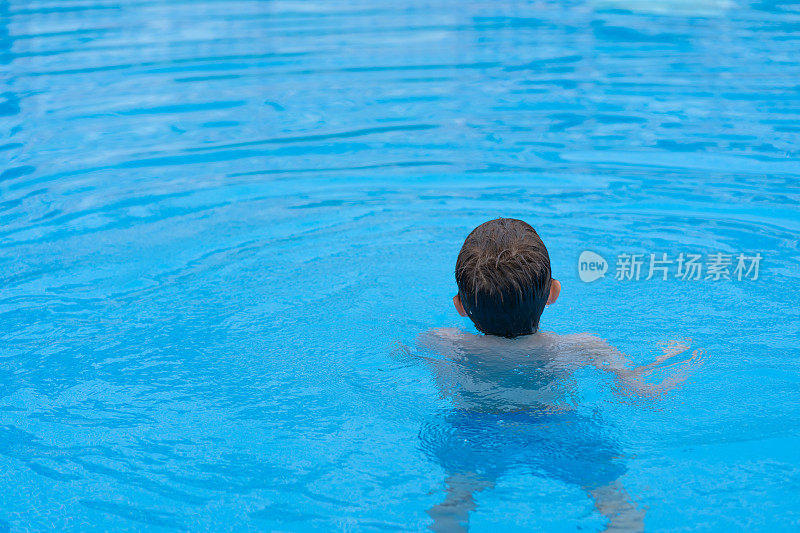 一个孩子在游泳池的水里，背对着相机，放松地看着地平线