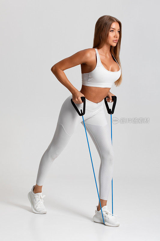 健身女性在灰色背景上用阻力带锻炼。运动女孩用伸展器锻炼