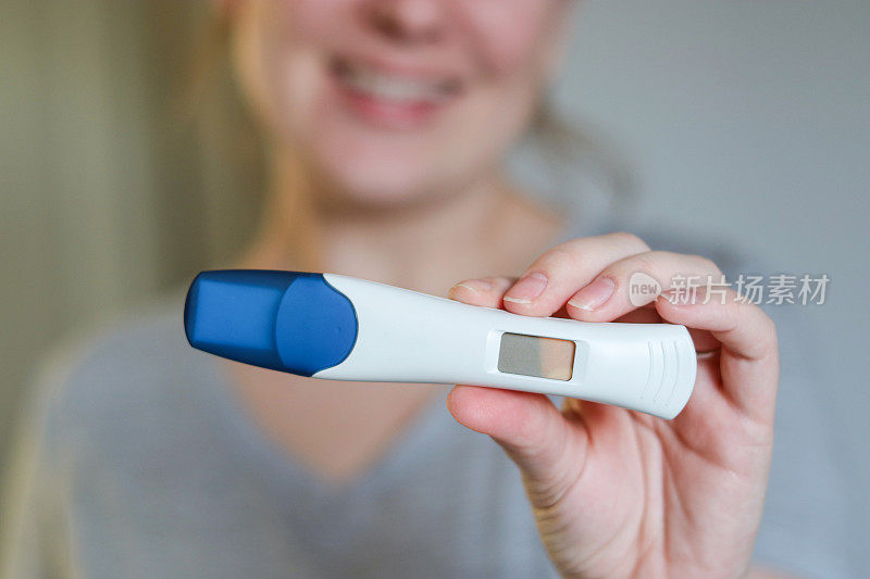 近距离俯视图，一个快乐的女人拿着数字阳性怀孕测试
