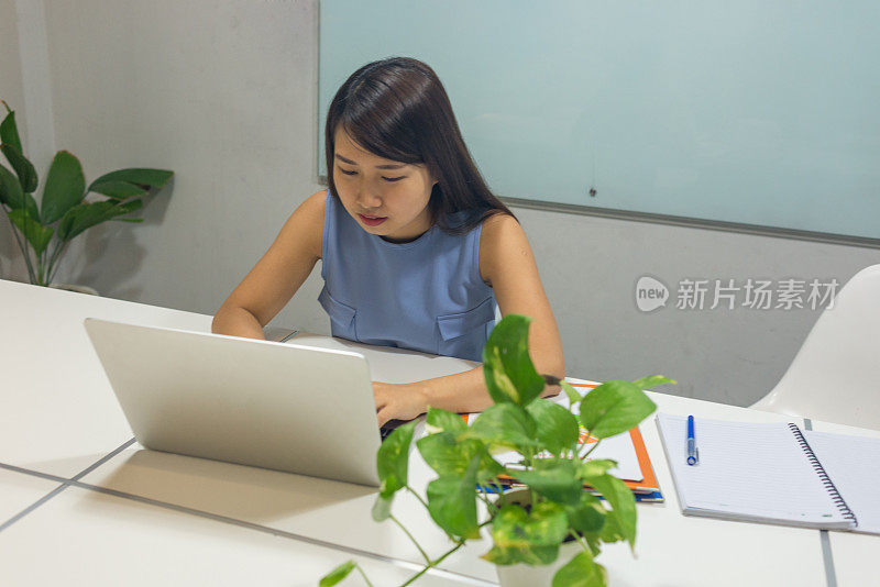 女人在笔记本电脑上打字，桌上放着植物和文件