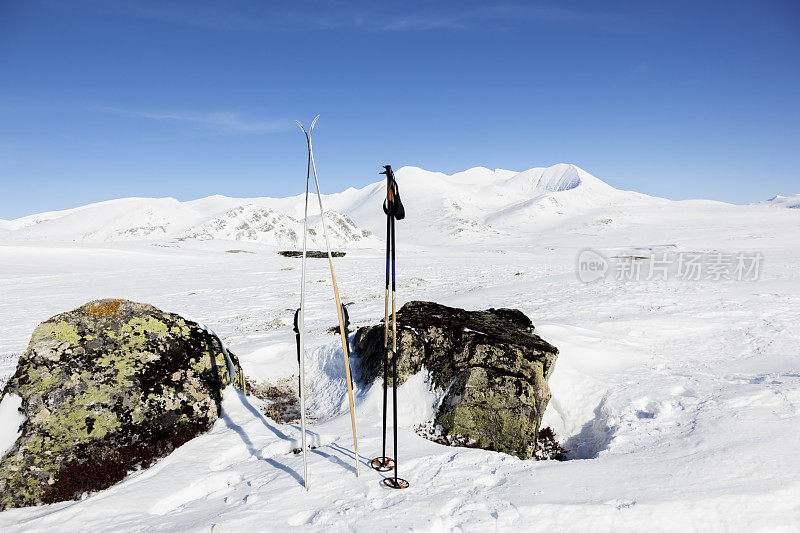 滑雪板和滑雪杆在多山的冬季景观与蓝色的天空。